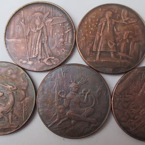 Puede incluir: Cinco monedas redondas de color cobre con diferentes diseños. Las monedas presentan un dragón, un árbol con un ciervo, una mujer con un pájaro, un hombre con un bastón y una mujer con un pájaro.