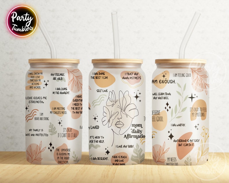 May include: Three stainless steel tumblers with a wood lid and a clear straw. Each tumbler features a different design with abstract shapes, flowers, and stars. The tumblers have positive affirmations printed on them, such as "I am enough", "Love gives me strength", and "I am doing the best I can".