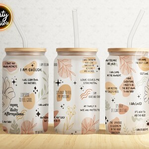 May include: Three white tumblers with a wood lid and a clear straw. Each tumbler has a different design with positive affirmations and abstract shapes in shades of brown, pink, and beige.