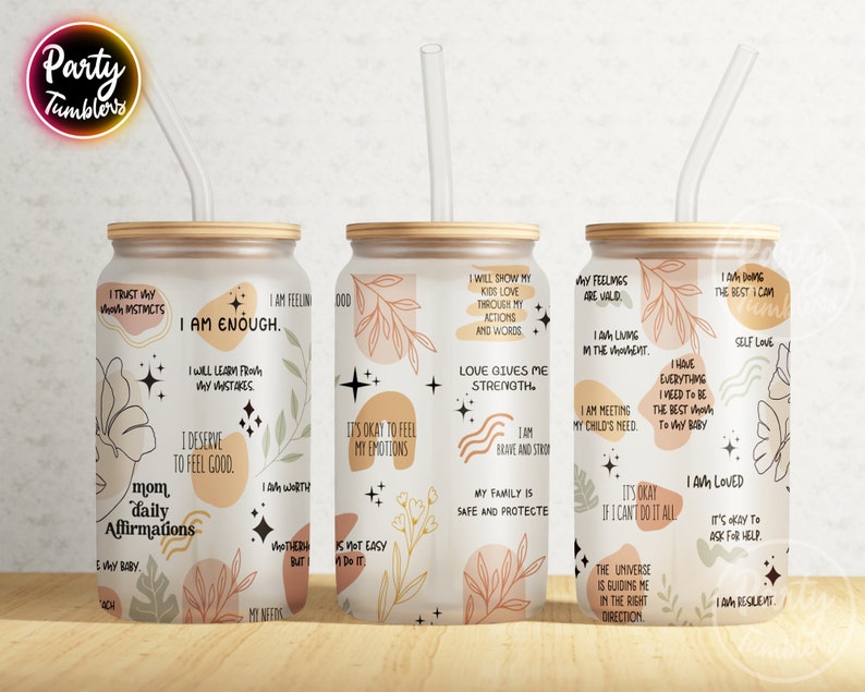 May include: Three white tumblers with a wood lid and a clear straw. Each tumbler has a different design with positive affirmations and abstract shapes in shades of brown, pink, and beige.