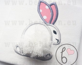 May include: White embroidered bunny with gray ears and pink polka dot accents. The bunny has a white tulle tail and is surrounded by a gray circle with a pink heart and the letter "b".