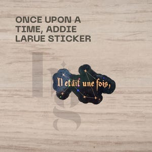 May include: A sticker with the text "ONCE UPON A TIME, ADDIE LARUE STICKER" at the top. Below is a dark blue sticker with the French phrase "Il était une fois" and a constellation design.