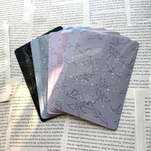 May include: A stack of holographic stickers featuring a repeating pattern of bats and stars on a light purple background. The stickers are arranged in a fan shape, with the top sticker partially covering the stickers below.