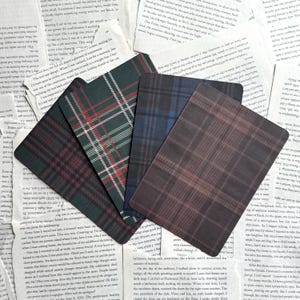 May include: A collection of five rectangular cards with plaid patterns in shades of green, blue, and brown. The cards are arranged on a background of printed paper, creating a vintage aesthetic. The plaid designs vary in color and pattern.