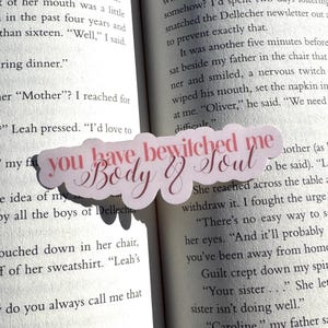May include: A pink and white sticker with the text "You have bewitched me body & soul" in a cursive font. The sticker is placed on a book.