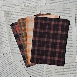May include: A stack of rectangular cards with plaid patterns in shades of red, orange, brown, and white. The cards are arranged on a background of aged paper with visible text.