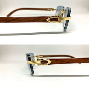 May include: A pair of sunglasses with a wooden frame and gold accents. The lenses are a light blue color.