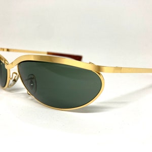 May include: Gold-tone aviator sunglasses with green lenses. The sunglasses have a thin metal frame and a curved, oval shape.