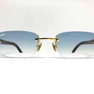 May include: Gold-tone Cartier sunglasses with a blue gradient lens. The sunglasses have a rectangular frame and a Cartier logo on the left temple.