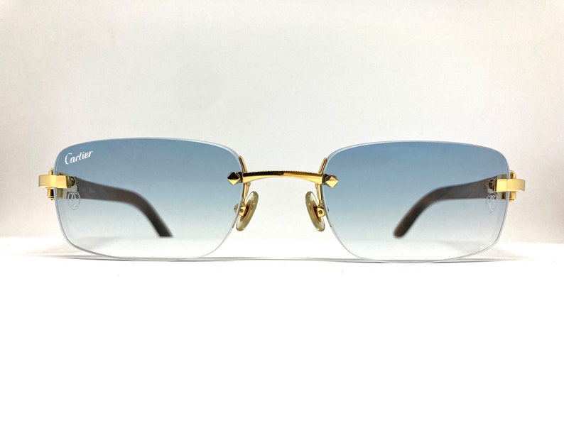 May include: Gold-tone Cartier sunglasses with a blue gradient lens. The sunglasses have a rectangular frame and a Cartier logo on the left temple.