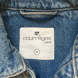May include: A white label with the text "Courr&egrave;ges Paris" and a size 30 tag attached to a blue denim jacket.