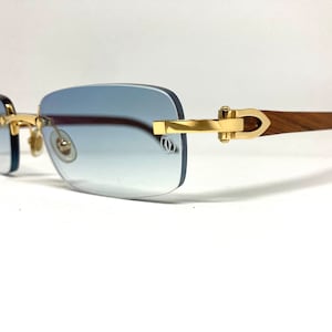 May include: Gold-tone rimless sunglasses with a wood temple and blue gradient lenses.