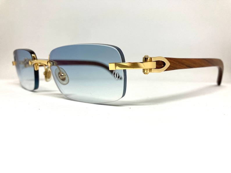 May include: Gold-tone rimless sunglasses with a wood temple and blue gradient lenses.
