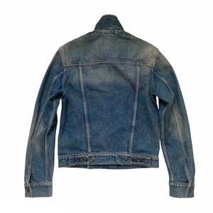 May include: A blue denim jacket with a classic design. The jacket has a button-up front, two chest pockets, and two front pockets.
