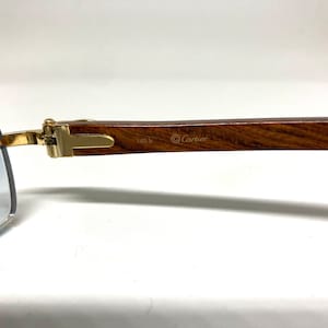 May include: A pair of gold-tone Cartier sunglasses with a brown wooden arm. The arm is engraved with the Cartier logo and the text "140 b".