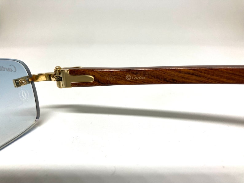 May include: A pair of gold-tone Cartier sunglasses with a brown wooden arm. The arm is engraved with the Cartier logo and the text "140 b".
