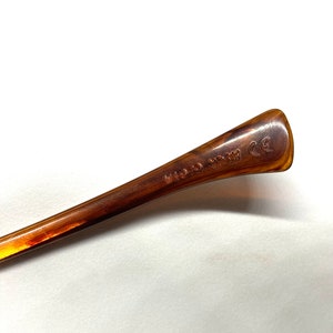 May include: Close-up of the brown plastic arm of a pair of glasses. The arm is marked with the text "Made in Italy" and "CE".