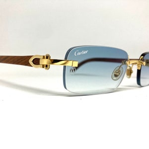 May include: A pair of gold-rimmed sunglasses with a wooden frame and blue gradient lenses. The sunglasses have a Cartier logo on the right lens.