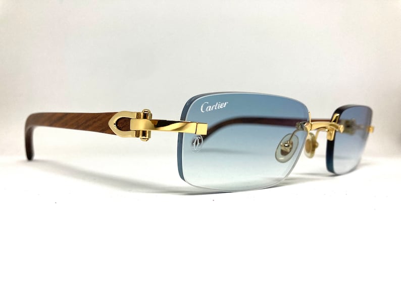May include: A pair of gold-rimmed sunglasses with a wooden frame and blue gradient lenses. The sunglasses have a Cartier logo on the right lens.