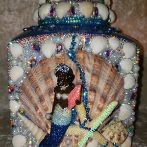 May include: A blue and white decorative box with a mermaid figurine, seashells, and starfish. The box is covered in iridescent rhinestones and has a crown-shaped lid.