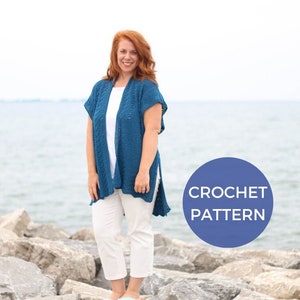 May include: A woman wearing a teal blue crochet cardigan with a white top and white trousers. The cardigan has a loose fit and a slightly open front. The woman is standing on a rocky beach with a blue circle behind her that says "CROCHET PATTERN".