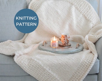 May include: A white knitted throw blanket draped over a light blue sofa with a candle and a mug on a wooden tray. The text "Knitting Pattern" is on a blue circle in the top left corner of the image.