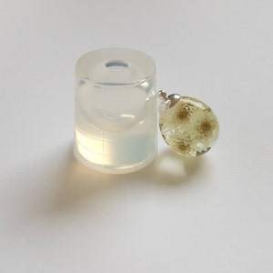 May include: A clear silicone mold for resin casting, next to a finished resin pendant with dried white flowers inside.