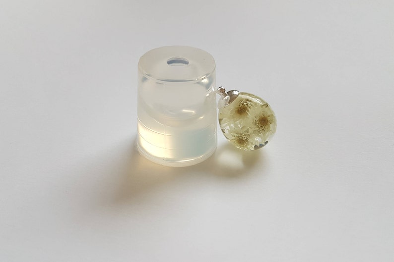 May include: A clear silicone mold for resin casting, next to a finished resin pendant with dried white flowers inside.