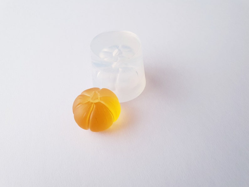 May include: A clear silicone mold for making small pumpkin-shaped resin crafts. A finished pumpkin-shaped resin piece is shown next to the mold.