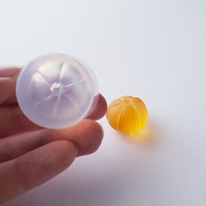 May include: A clear silicone mold shaped like a pumpkin, next to a small orange pumpkin-shaped resin piece.