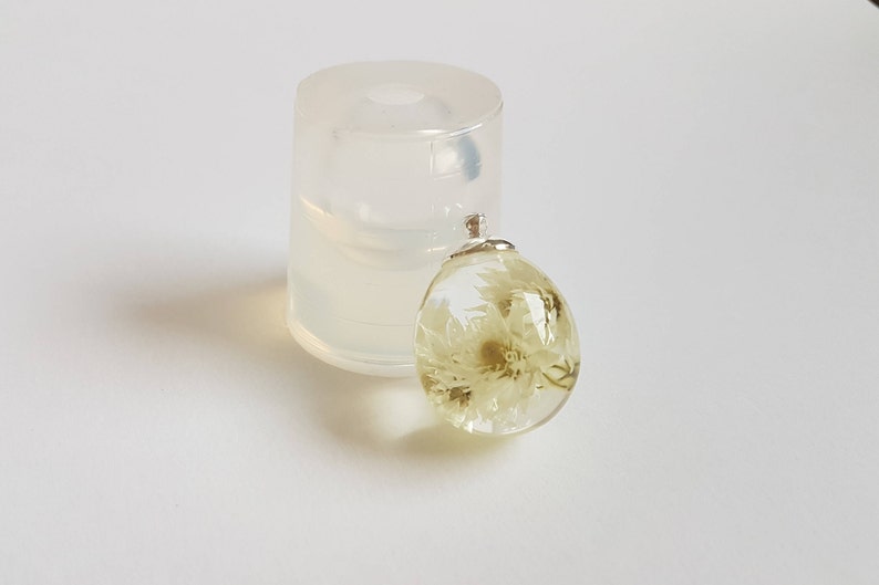 May include: A clear resin pendant with a dried white flower inside. The pendant is attached to a silver bail.