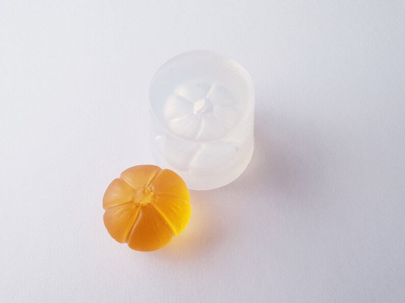 May include: A clear silicone mold shaped like a pumpkin, with a smaller orange pumpkin made from resin sitting next to it.