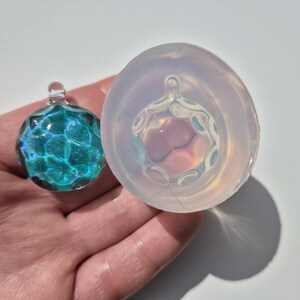 May include: A clear silicone mould for making a round pendant with a textured surface. The mould is shown with a finished pendant made of blue and green glass.