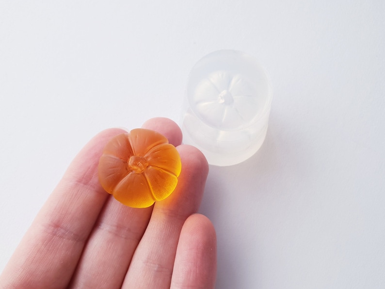 May include: A clear silicone mold for making small pumpkin-shaped resin crafts. A finished pumpkin made with resin is shown in the mold.