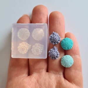 May include: A clear silicone mould with four impressions of sea urchins. There are three sea urchin shaped resin pieces in turquoise, teal, and purple.