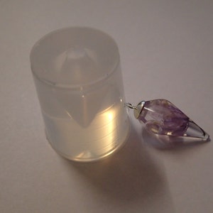 May include: A clear plastic mold for making a pendant, next to a purple amethyst crystal pendant.
