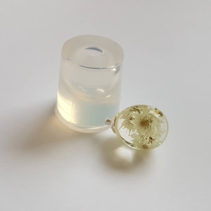 May include: A clear round resin sphere with dried white flowers inside. The sphere is sitting next to a clear silicone mold.