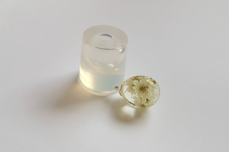 May include: A clear round resin sphere with dried white flowers inside. The sphere is sitting next to a clear silicone mold.