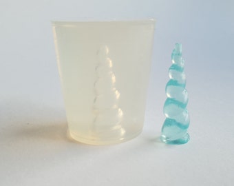 May include: A clear, cylindrical mold with a spiral design and a small, light blue, spiral-shaped object. The mold is made of a translucent material, and the object is a solid, smooth, and glossy material. The objects are on a white surface.