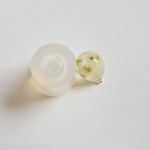 May include: A clear silicone mold for making resin jewelry, with a round, flat base and a raised ring in the center. Next to the mold is a small, round, clear resin pendant with dried white flowers inside.