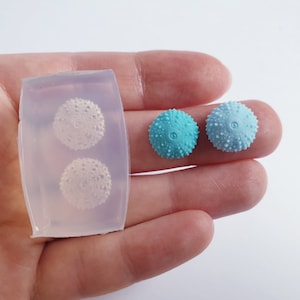 May include: Two silicone moulds for making sea urchin shaped resin earrings. The moulds are clear and have two cavities each. Two finished resin earrings are shown, one is light blue and the other is a darker blue.