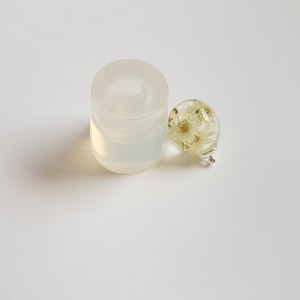 May include: A clear silicone mold for making round resin ornaments, next to a finished round resin ornament with dried white flowers inside.
