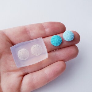 May include: A silicone mould for making sea urchin shaped resin earrings. The mould is shown with two finished resin earrings in light blue and turquoise.