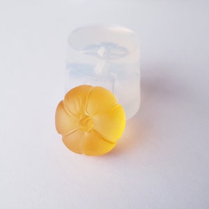 May include: A yellow resin flower charm with a detailed design. The charm is sitting next to a clear silicone mold.