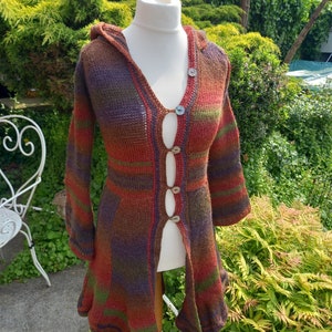 May include: A long, hooded cardigan with a colourful striped pattern in shades of brown, red, purple, and green. The cardigan has a front opening with buttons and a flowing hemline.