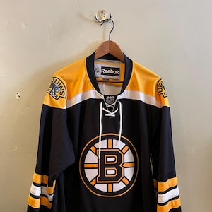 May include: Black and gold hockey jersey with the Boston Bruins logo and Reebok branding.
