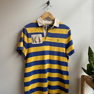 May include: A set of three ceramic mugs with a speckled, cream-colored glaze. Each mug features a different hand-painted design: a blue and green leaf, a yellow flower, and a red berry. The mugs have a simple, rounded shape.