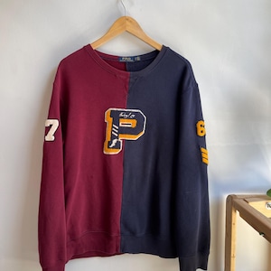 May include: A two-tone sweatshirt, split vertically with burgundy and navy blue. The burgundy side features a white number 7, while the navy side has a white number 6 and yellow stripes. A large letter "P" is centered on the chest.