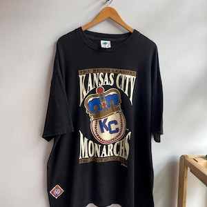 Peut inclure: T-shirt noir avec le logo des Kansas City Monarchs, une équipe de baseball des Negro Leagues. Le design comprend une couronne, les lettres "KC" et les mots "Monarchs" et "The Spirit of the Past".