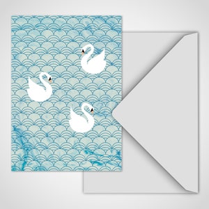 Può includere: Un biglietto di auguri con un motivo blu e bianco con tre cigni bianchi. Il biglietto è accompagnato da una busta bianca. Il design ha un effetto acquerello, con un motivo a onde.